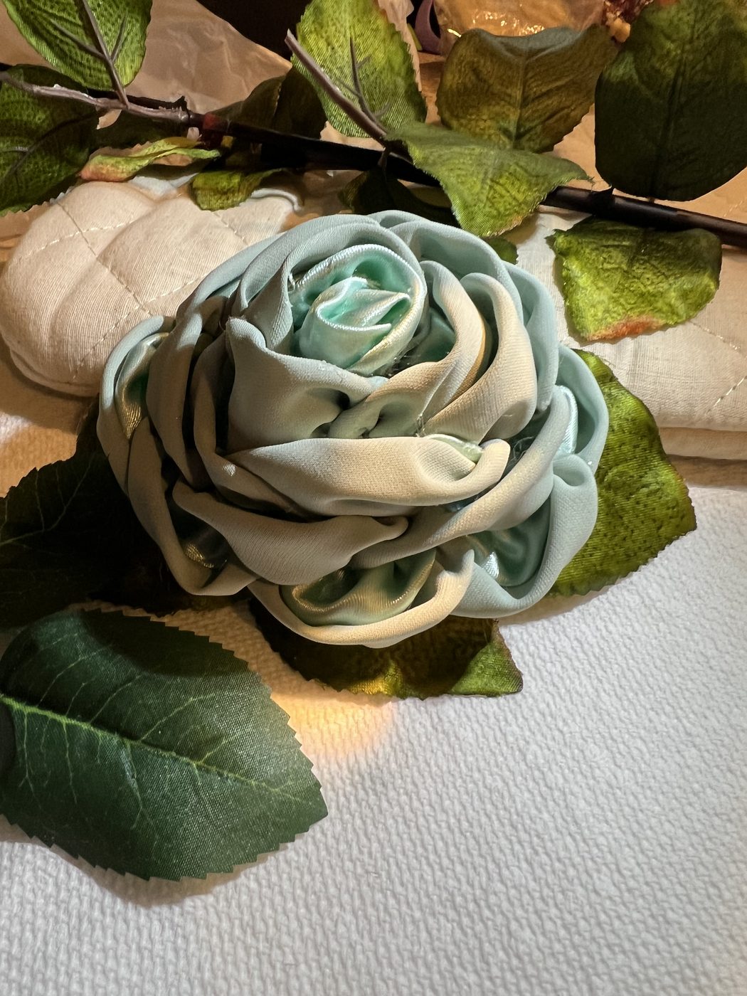 Handmade sage green ribbon rose among leaves